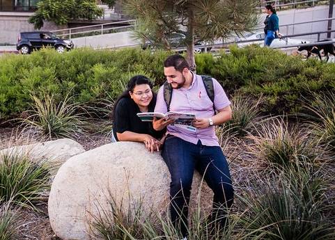 Two students outside on the city college campus looing at a book