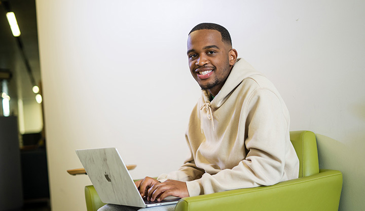 An man sits in a green chair and works on a laptop