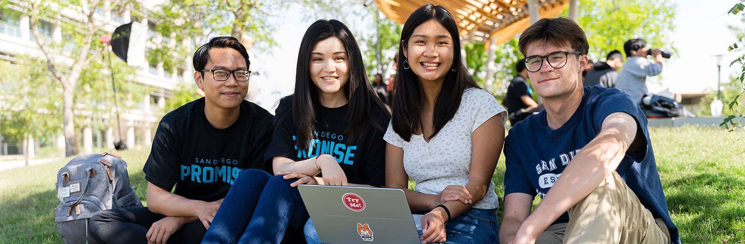 Four students sit on the grass in the Mesa Quad. One is using a laptop