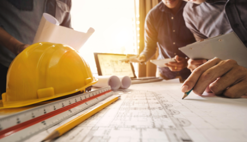 A close up of a construction hat and blue prints on a table