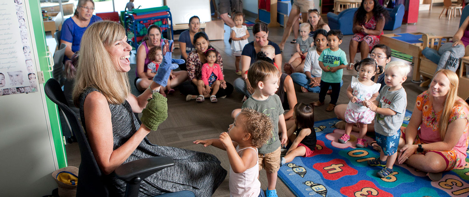 An instructor uses puppets to entertaing a group of children sitting on the floor