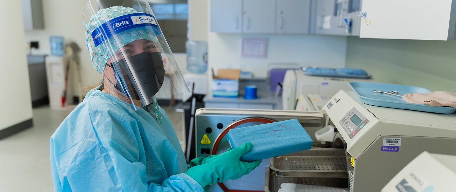 A student in full protective medical gear puts a tray into a machine